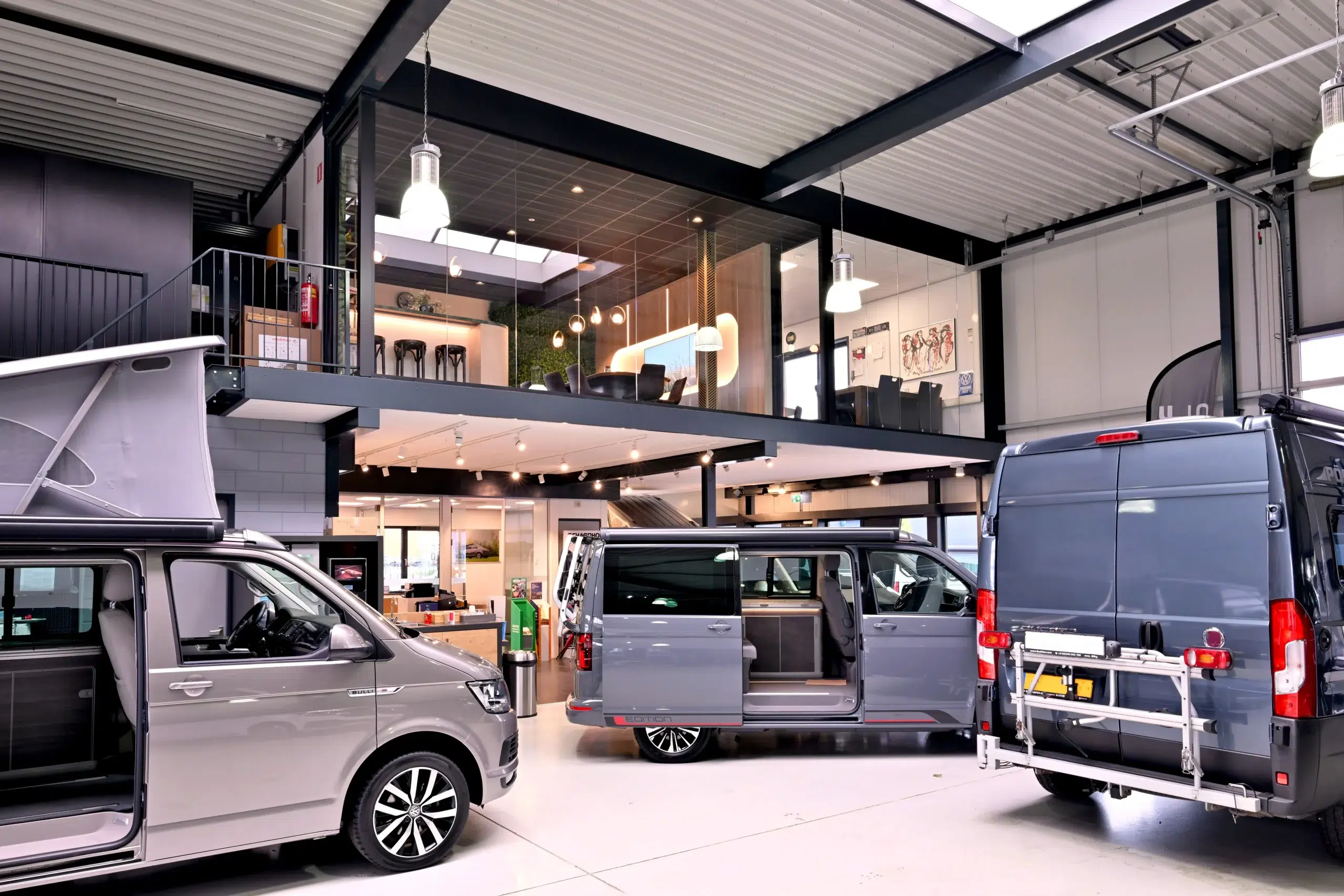 Overzicht van de showroom en werkplaats van Scharphof Campers met meerdere campers en zicht op de moderne wachtruimte op de verdieping